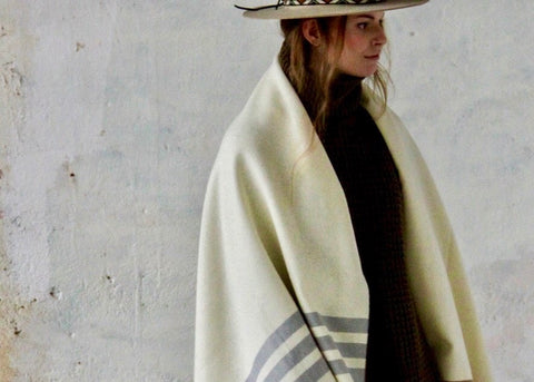 PICTURE OF STOLA LORIGA, MADE IN BEAUTIFUL WOOLWHITE. THE PONCHO IS MADE IN 50% BIO COTTON, 50% BIO WOOL. STRIPED DETAILS IN BEIGE AND (DARK) GREY. DESIGNED BY SCHOOLOFLIFEPROJECTS IN ARNHEM AND PRODUCED IN THE HEART OF PORTUGAL.
