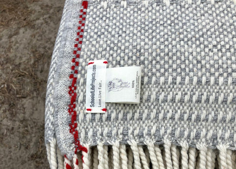 Detail from the etiquette with blanket Manteigas, SchoolofLifeProjects, made in 100% bio wool. Colors wool white, grey melange and bright red