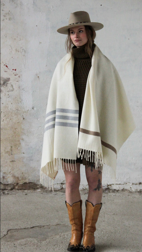 PICTURE OF STOLA LORIGA, MADE IN BEAUTIFUL WOOLWHITE. THE PONCHO IS MADE IN 50% BIO COTTON, 50% BIO WOOL. STRIPED DETAILS IN BEIGE AND (DARK) GREY. DESIGNED BY SCHOOLOFLIFEPROJECTS IN ARNHEM AND PRODUCED IN THE HEART OF PORTUGAL.