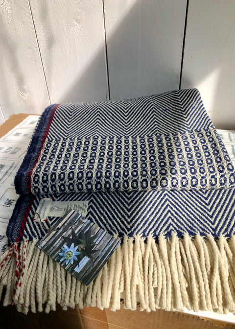 DETAIL OF BLANKET BELMONTE; WEAVING PATTERNS; BIRD'S EYE AND TWILL PATTERN. COLORS ARE WOOL WHITE AND NAVY BLUE. THE RED LISTING REMINDS OF THE SELVEDGE WHICH RUNS ALONG THE LONG SIDE OF THE BLANKET. THE PRODUCT IS PART OF THE SCHOOLOFLIFEPROJECTS COLLECTION AND IS MADE OF 100% WOOL FROM THE SHEEP WHICH ARE GRAZING IN THE SERRA DA ESTRELA NATIONAL PARK. DESIGNED IN ARNHEM, CLOSE TO DE HOGE VELUWE. 