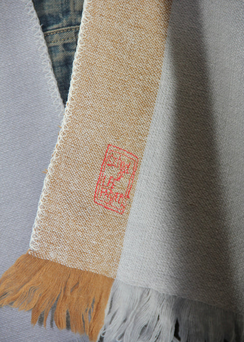 DETAIL OF DETAIL OF PONCO GUARDA, MADE IN TWO BEAUTIFUL COLORS; CLASSICAL BEIGE AND PALE BLUE. THE PONCHO IS MADE IN 50% BIO COTTON, 50% BIO WOOL. THE PONCHO HAS A RED LISTING, AND A BEAUTIFUL STAMP EMBROIDERED IN RED ON THE LEFT FRONT PANEL (FOR THE WEARER)