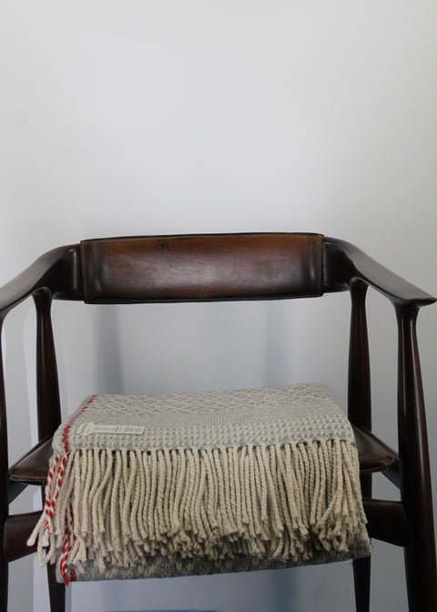 Our blanket Manteigas, folded on a chair, made out of Bio-wool. Made in heather grey, wool white and red listing (just as in denim!)